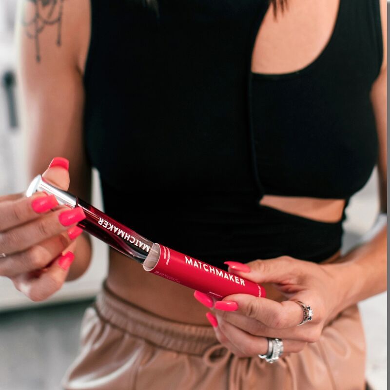 Persona che tiene in mano un flacone di profumo rosso con la scritta "MATCHMAKER" e una confezione rossa.