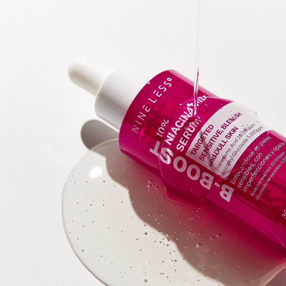 Flacone rosa di siero. Gocce di siero scorrono su una superficie. Scritta: NINE LESS, B-Boost, 10% Niacinamide Serum.