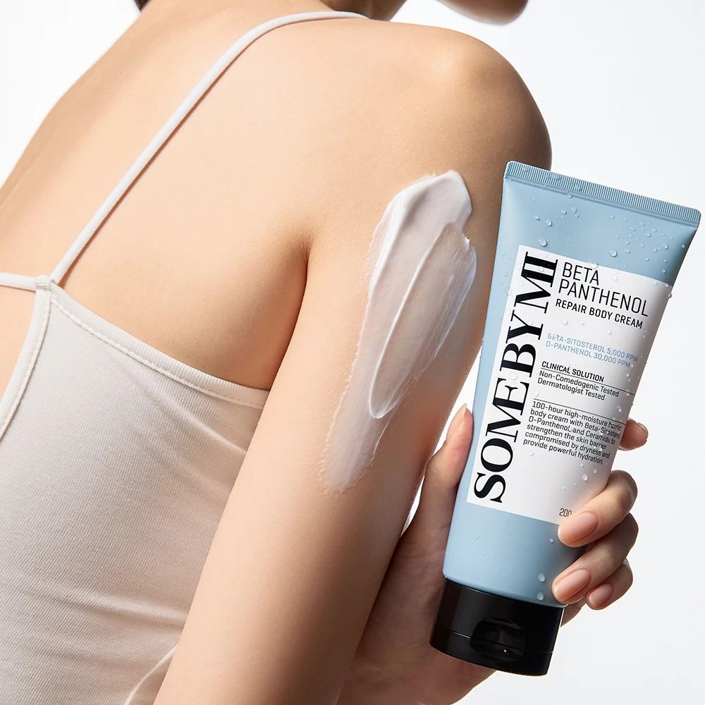 Pelle chiara con crema applicata. Tubo blu con tappo nero, nome del prodotto e testo. Crema sul braccio.