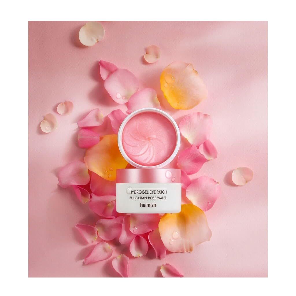 Vasetto bianco con coperchio rosa e patch occhi. Petali rosa e gialli circondano il prodotto. Scritta: Heimish, Hydrogel Eye Patch Bulgarian Rose Water.