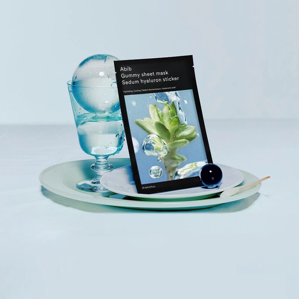 Abib Gummy Sheet Mask Sedum Hyaluron Sticker su un piatto con bicchiere e acqua.