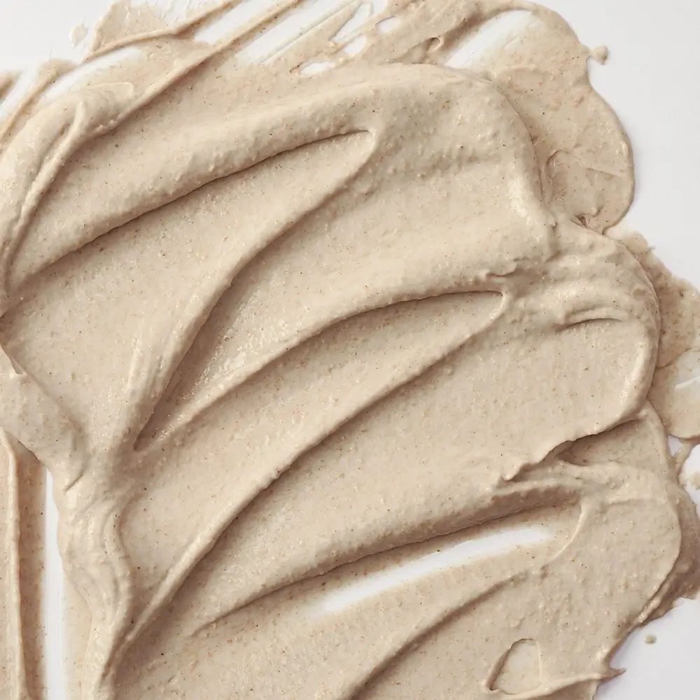 Primo piano di maschera viso cremosa beige. La texture è applicata a strisce ondulate.