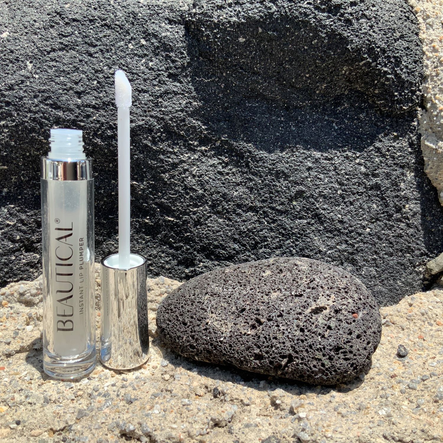 BEAUTICAL Instant Lip Plumper accanto a una pietra. L'applicatore è estratto dal tubo.