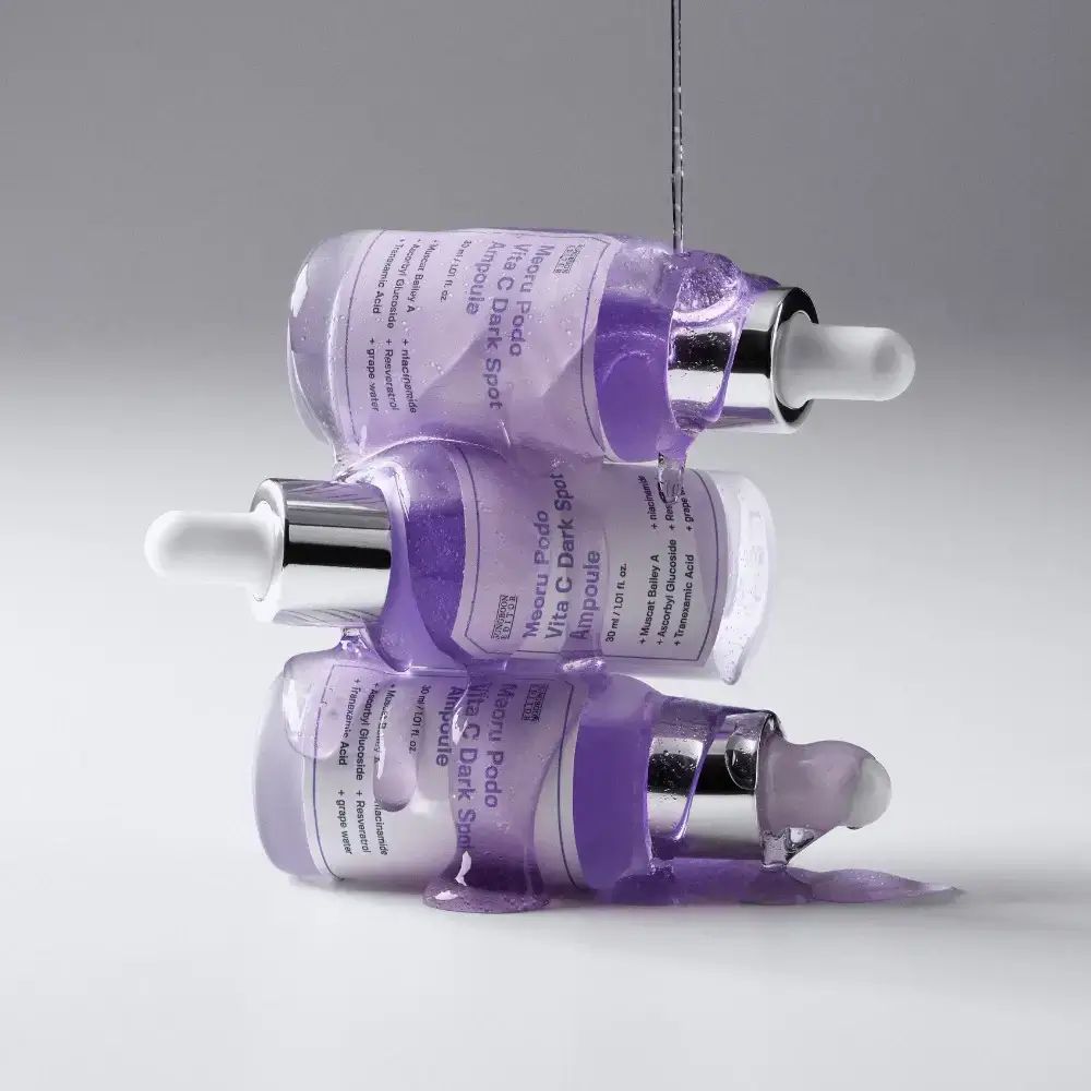 Tre flaconi SUNGBOON EDITOR Meoru Podo Vita C Dark Spot Ampoule. Liquido viola che gocciola. Tappi argentati, pipette bianche.