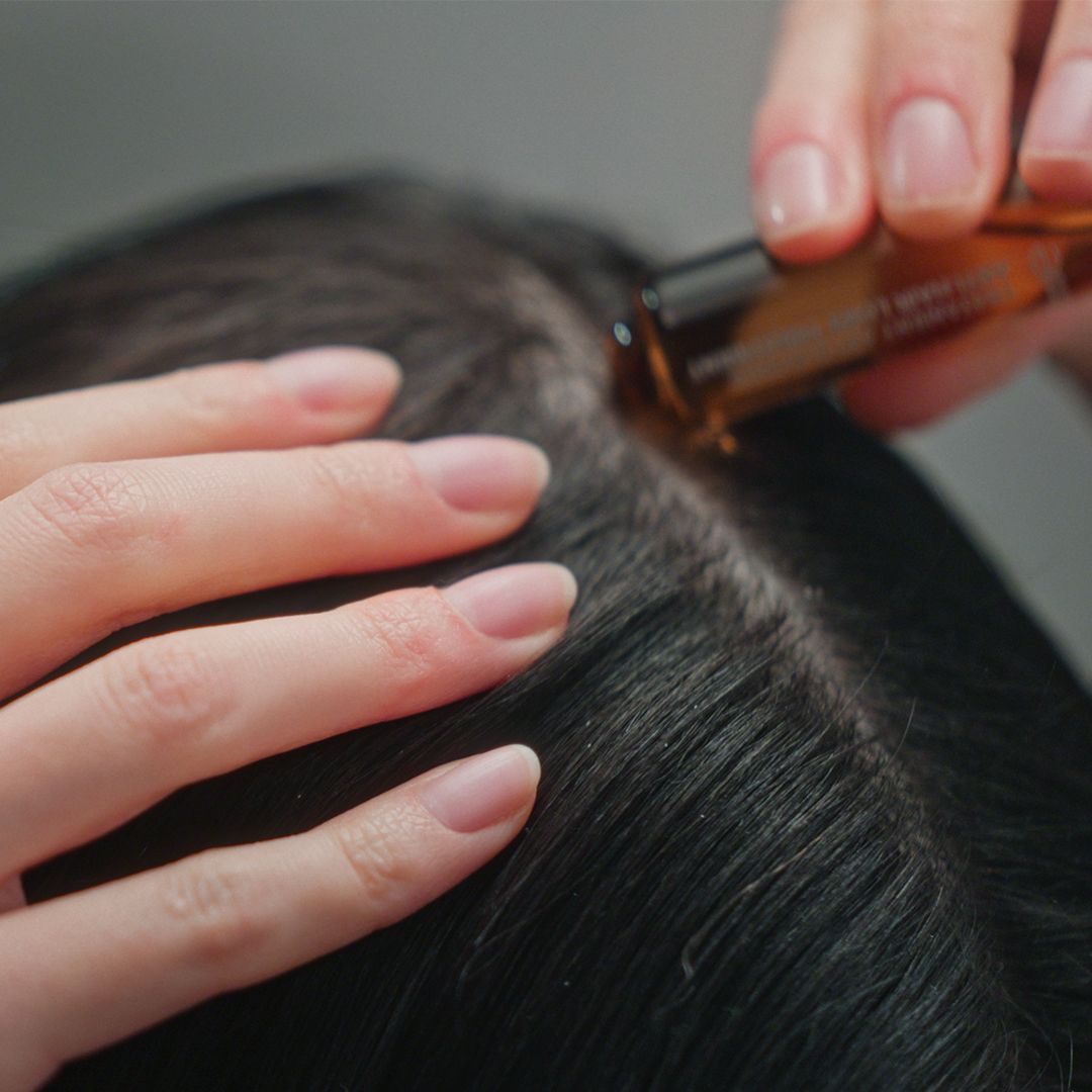 Mani applicano una fiala di liquido marrone sul cuoio capelluto.