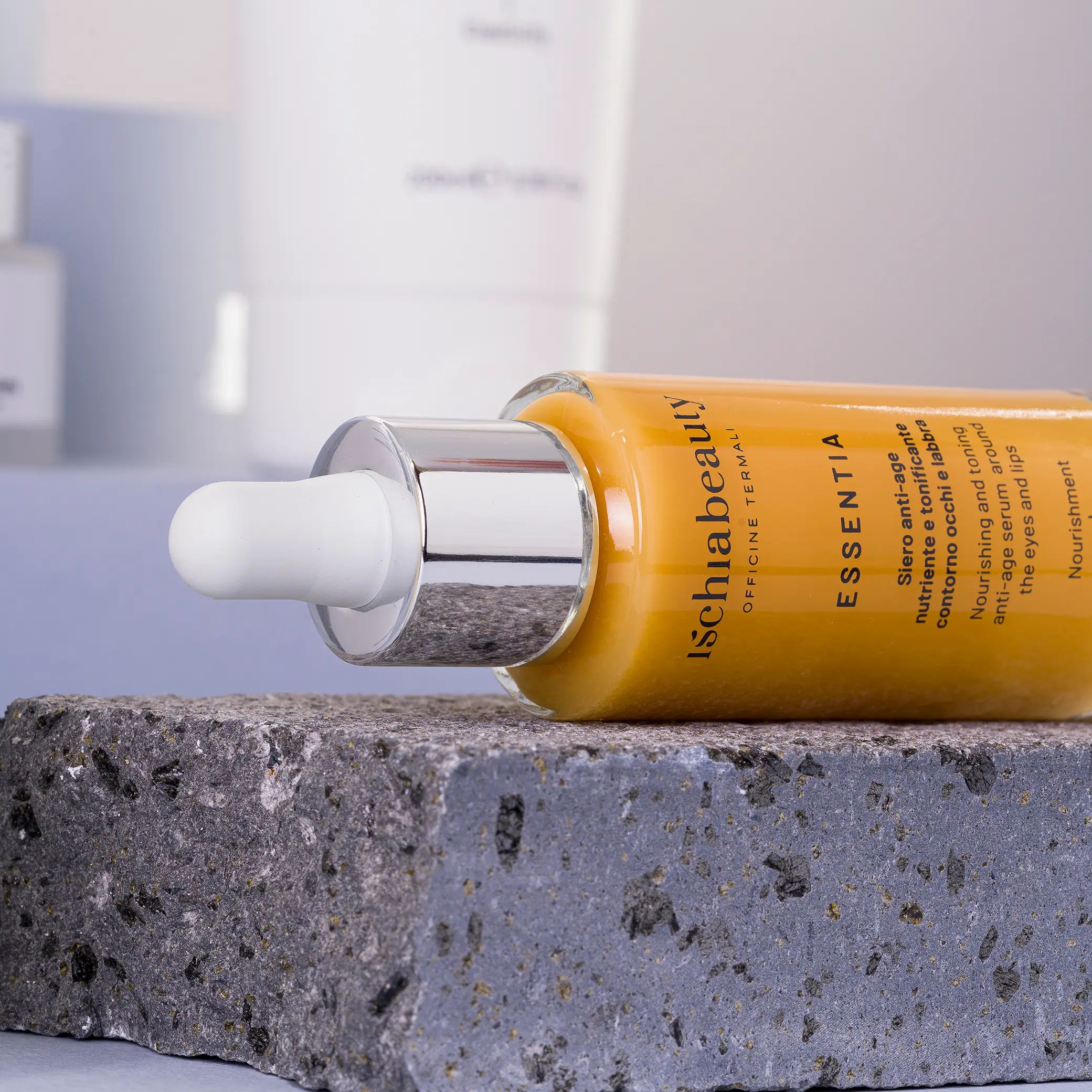 Flacone di siero ambrato con contagocce, appoggiato su pietra. Scritta: Ischiabeauty, Essentia, Siero anti-age.