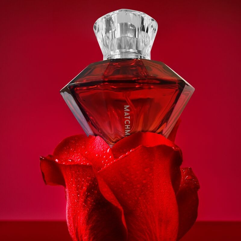 Flacone di profumo rosso a forma di diamante, posizionato su una rosa rossa con gocce d'acqua.