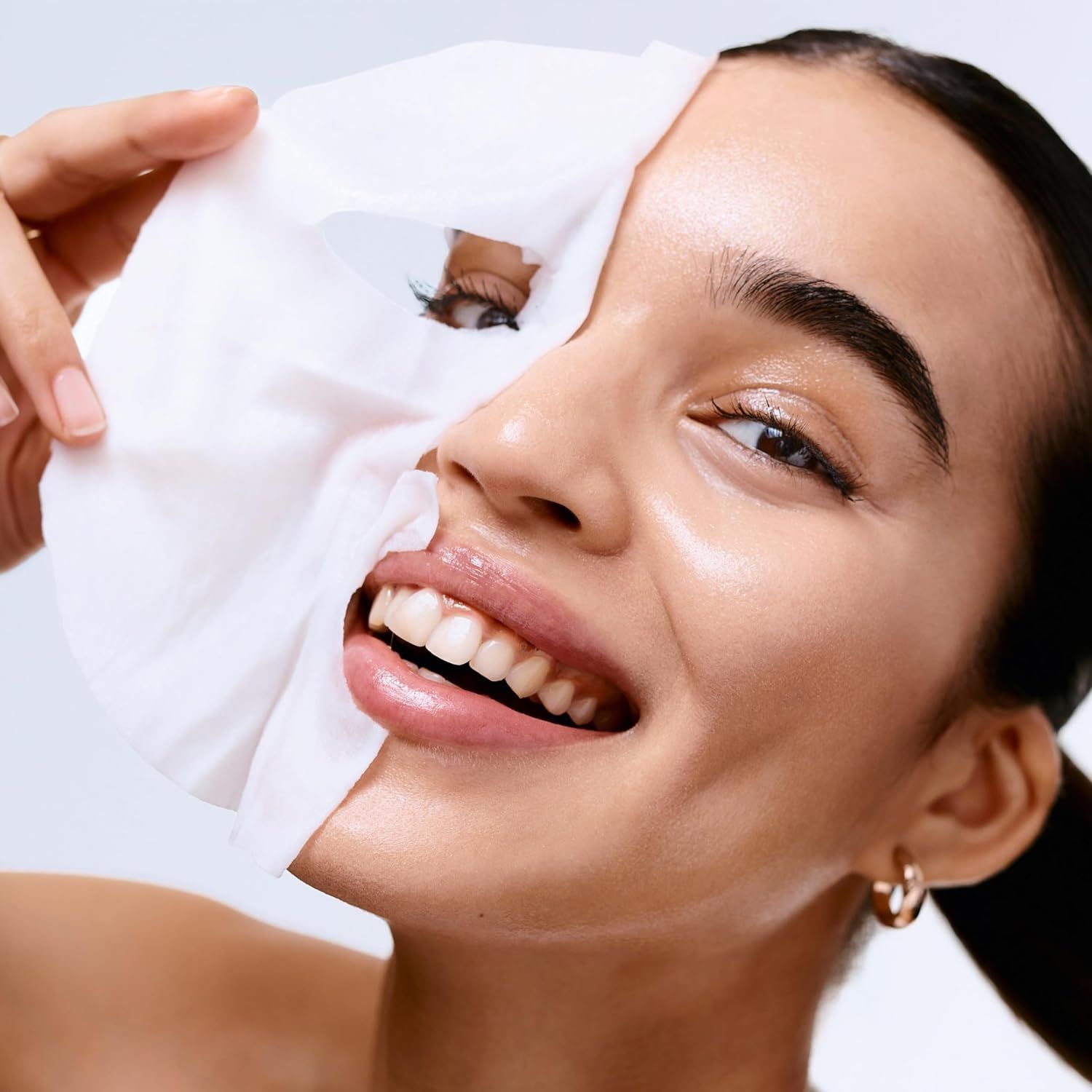 Donna tiene una maschera in tessuto davanti al viso. La maschera copre metà del viso. Sorride.