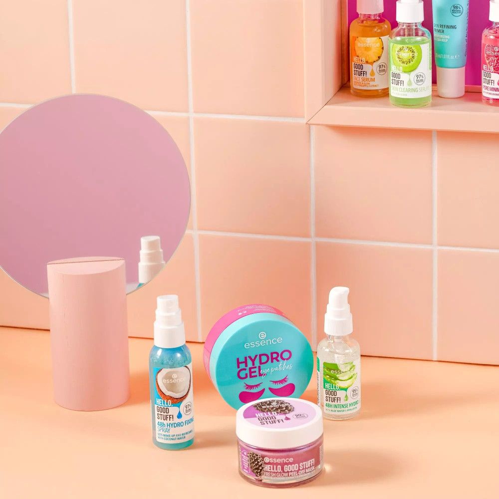 Vari prodotti cosmetici su piastrelle rosa. Tra cui: flacone spray con scritta Hello Good Stuff, Hydro Fixing Spray.