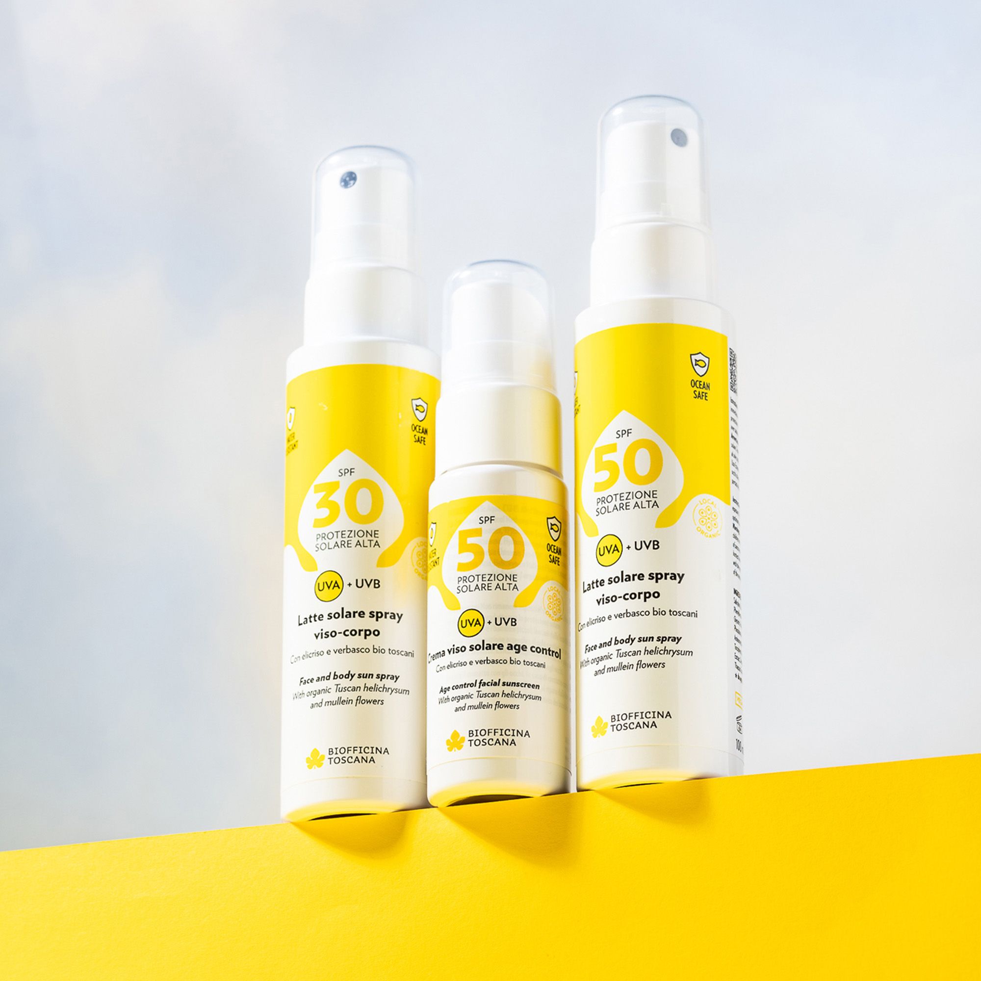 Tre flaconi spray bianchi con etichette gialle. Testo: SPF 30, SPF 50, protezione solare, UVA+UVB. Marchio: Biofficina Toscana. Su sfondo giallo.