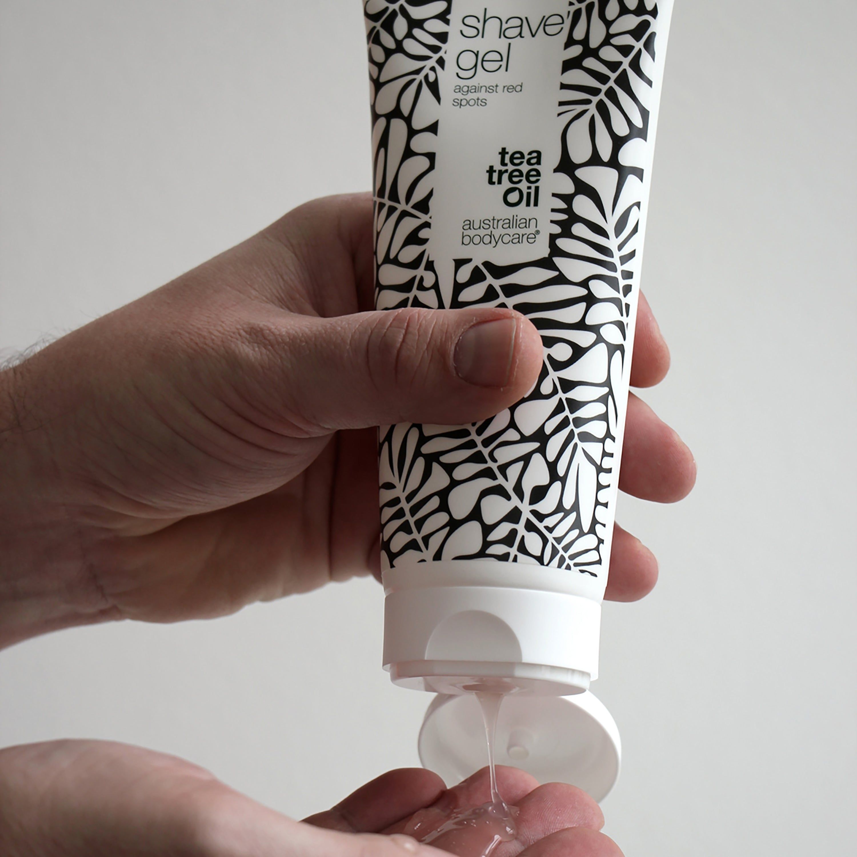 Persona che tiene in mano un tubo di gel da barba. Il gel viene premuto nella mano. Scritta: shave gel against red spots. Australian Bodycare.