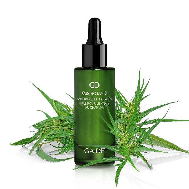 Flacone di vetro verde con contagocce nero, circondato da foglie di cannabis. Scritta: CB2 Botanic Cannabis Seed Facial Oil. Marchio: GA-DE.