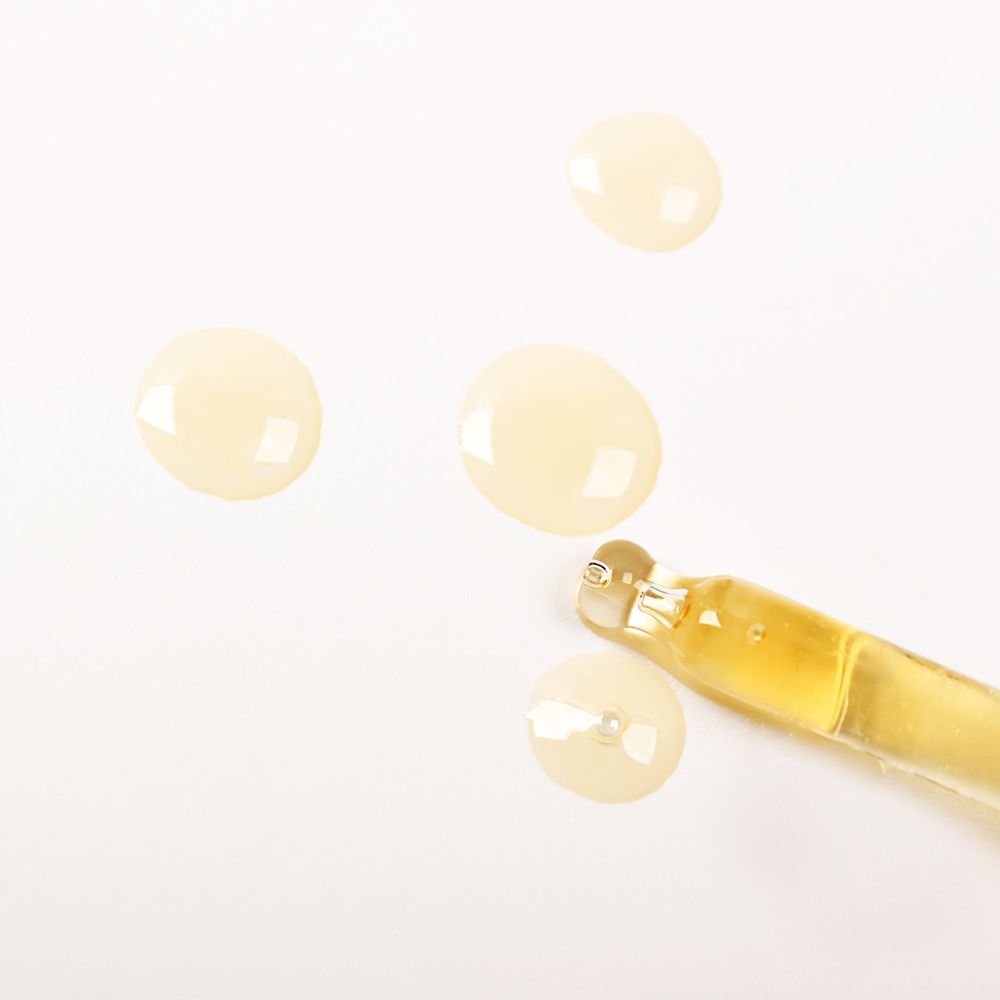 Gocce di olio di argan e pipetta su sfondo bianco. L'olio è giallastro.
