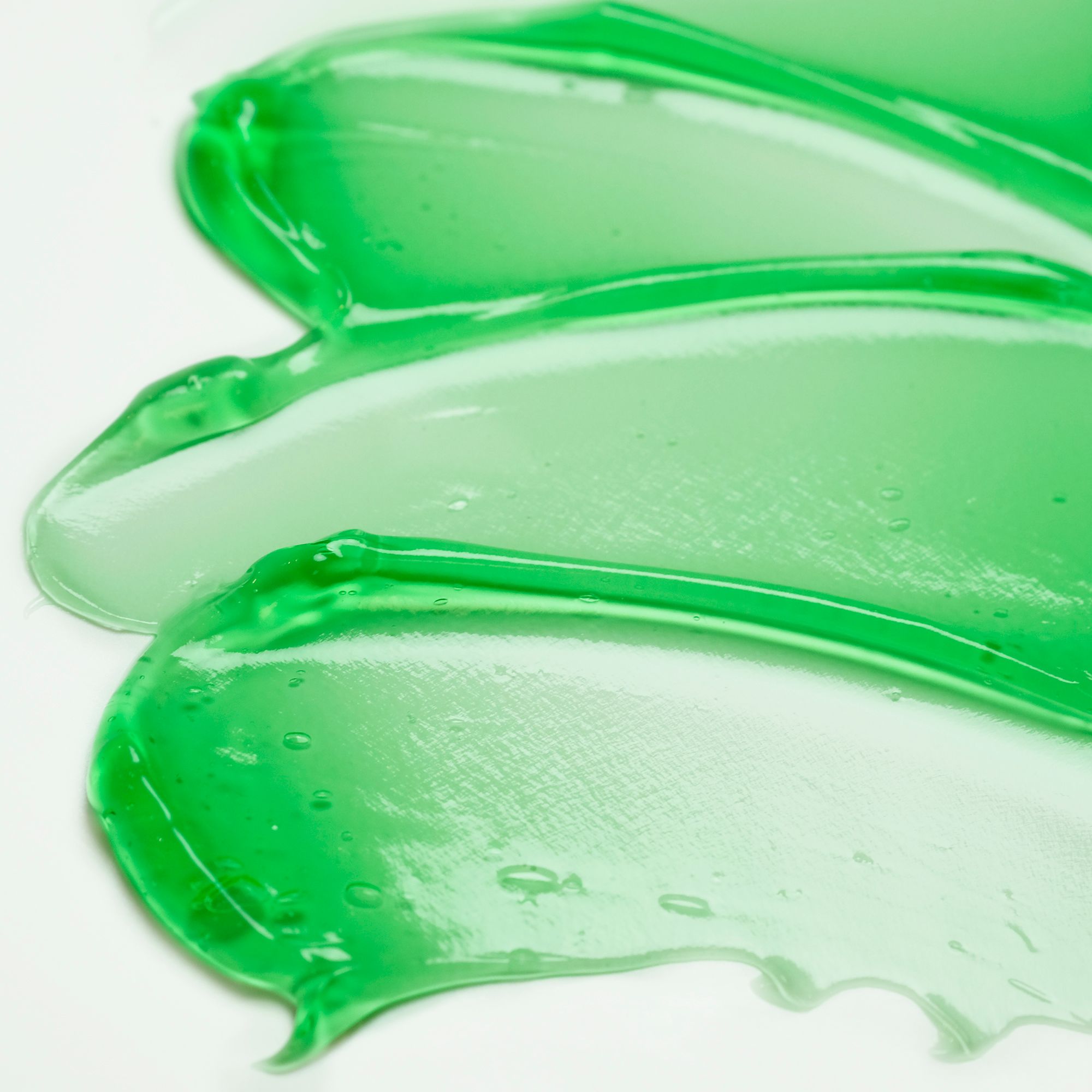 Strisce di gel verde su sfondo bianco. Texture chiara e trasparente. Alcune bolle visibili.