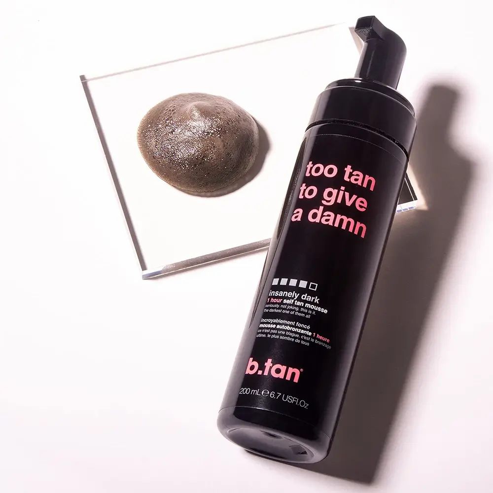 Flacone nero con testo e mousse abbronzante su specchio. Scritta: too tan to give a damn.