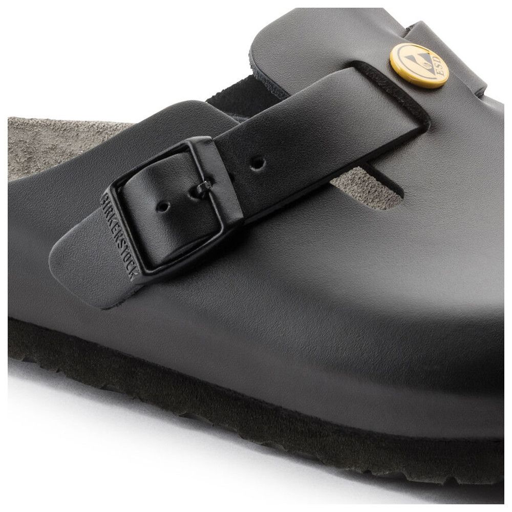 Primo piano dello zoccolo nero. Cinturino con fibbia e logo Birkenstock in rilievo. Dettaglio logo giallo.