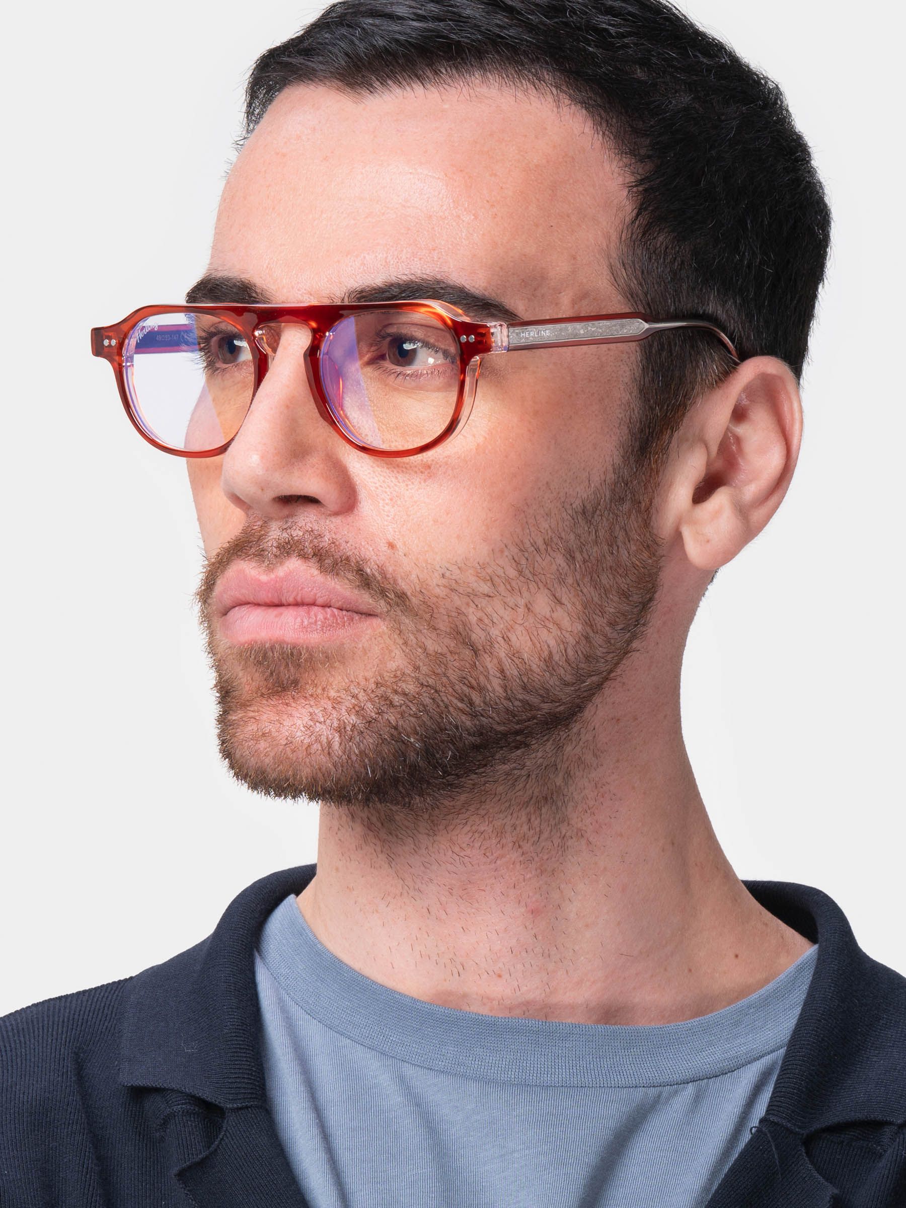 Uomo con occhiali rossi. Lenti rotonde, aste in metallo. L'uomo indossa una maglietta blu.