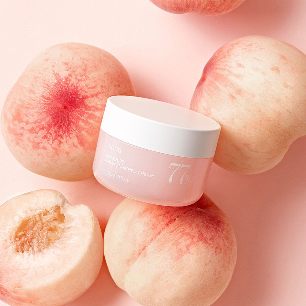 Vaso di crema rosa con coperchio bianco, circondato da pesche. Scritta: Anua, PEACH 77, Niacin Enriched Cream, 77%.