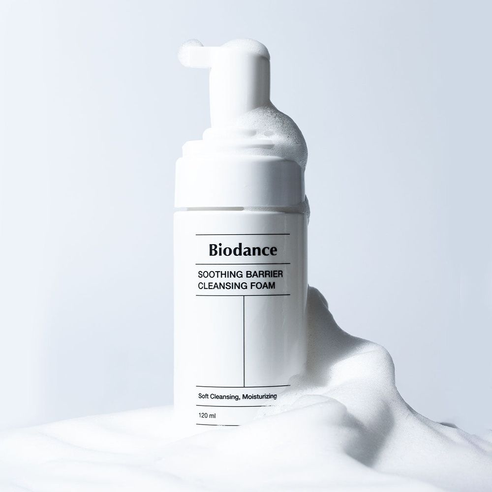 Flacone bianco con schiuma. Scritta: BIODANCE, SOOTHING BARRIER CLEANSING FOAM. Schiuma intorno al flacone.