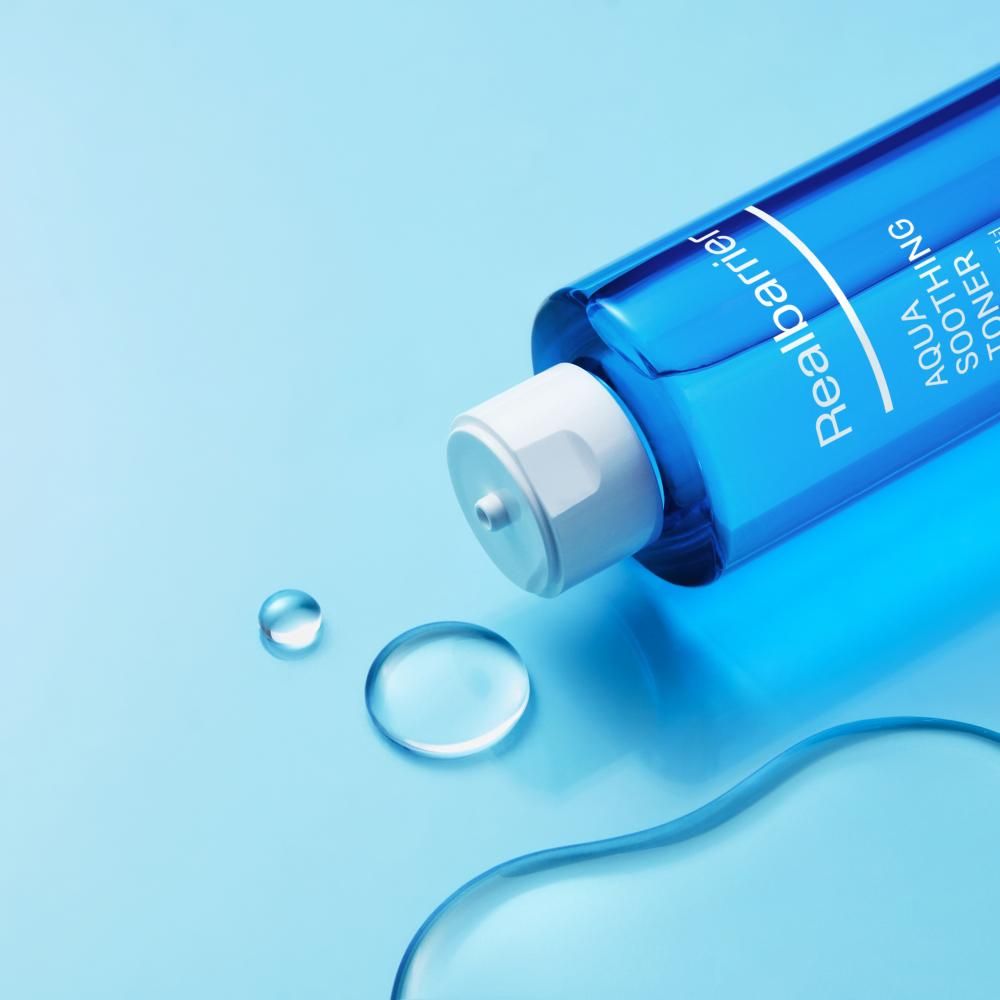 Flacone blu coricato. Accanto gocce d'acqua. Scritta: Realbarrier, AQUA SOOTHING TONER.