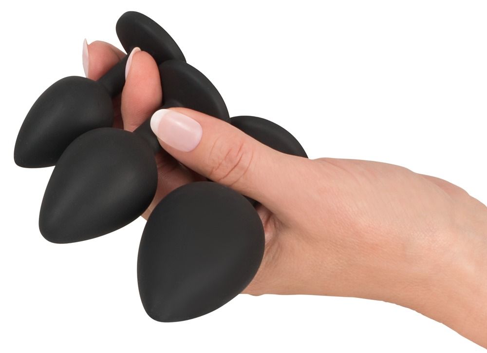 Mano che tiene una selezione di plug anali neri. Diverse dimensioni e forme.