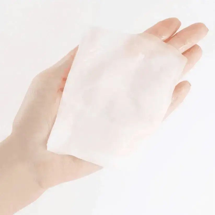 Maschera in tessuto idratante tenuta in mano. Forma rettangolare, bianca, leggermente trasparente.