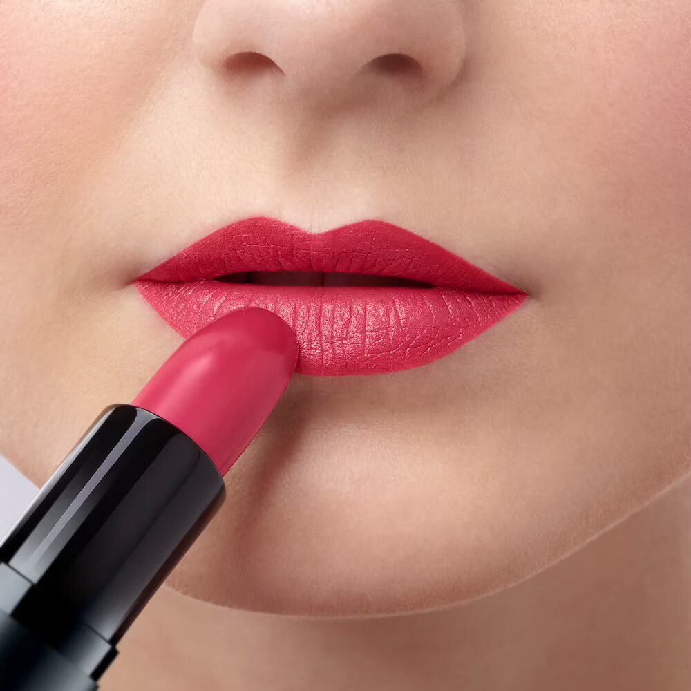 Persona che applica rossetto rosa. Portarossetto nero visibile.