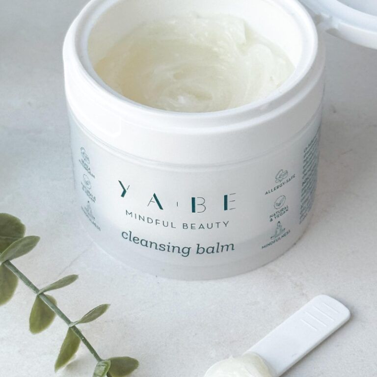 Vasetto bianco con coperchio aperto. Contenuto visibile. Scritta: YA.BE, Mindful Beauty, Cleansing Balm. Spatola.