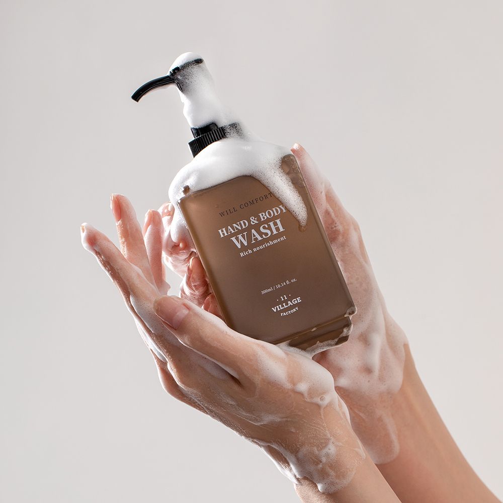 Mani che tengono un flacone con schiuma. Scritta: WILL COMFORT HAND & BODY WASH. Marchio: VILLAGE 11 FACTORY.