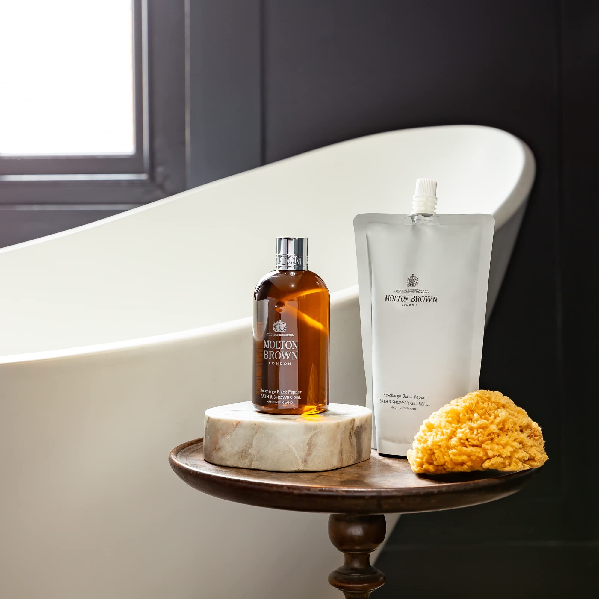 Vasca da bagno, tavolo con prodotti Molton Brown e spugna. Bottiglia e ricarica.