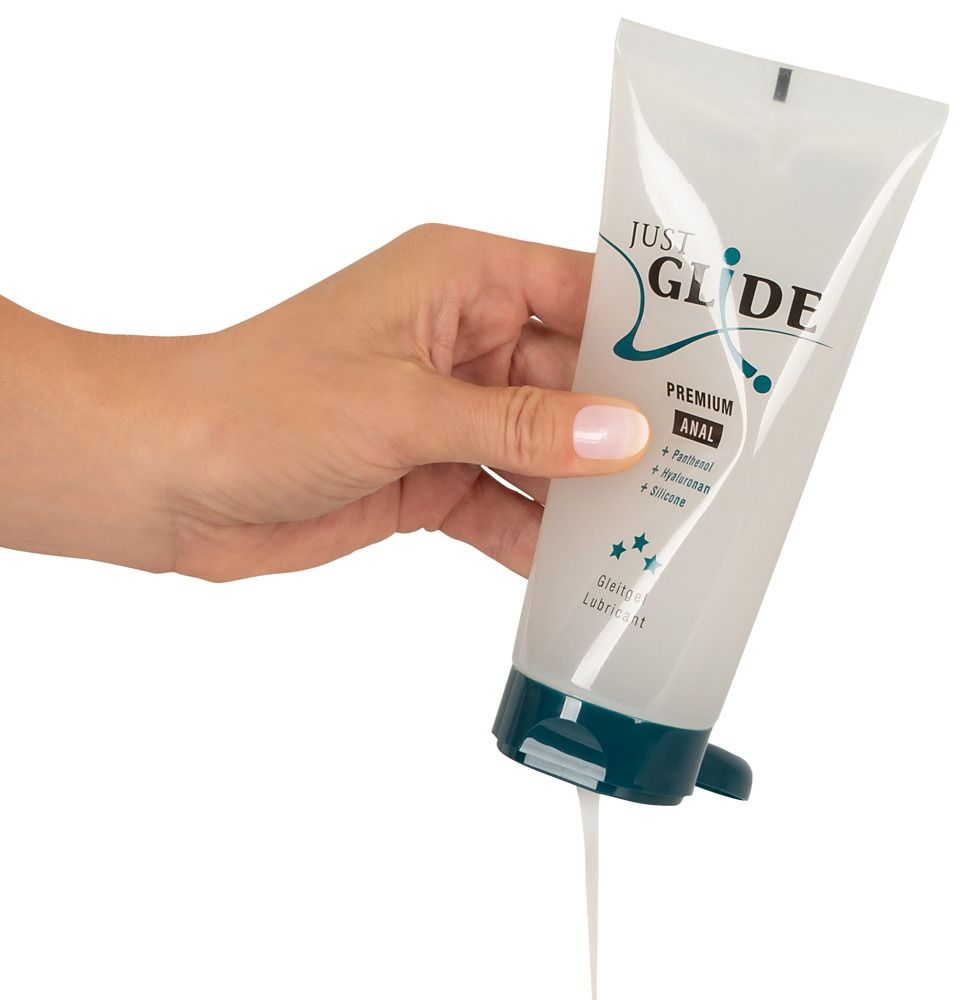 Mano che tiene un tubo di gel lubrificante. Il gel fuoriesce dall'apertura. Scritta: JUST GLIDE PREMIUM ANAL. Tappo blu.