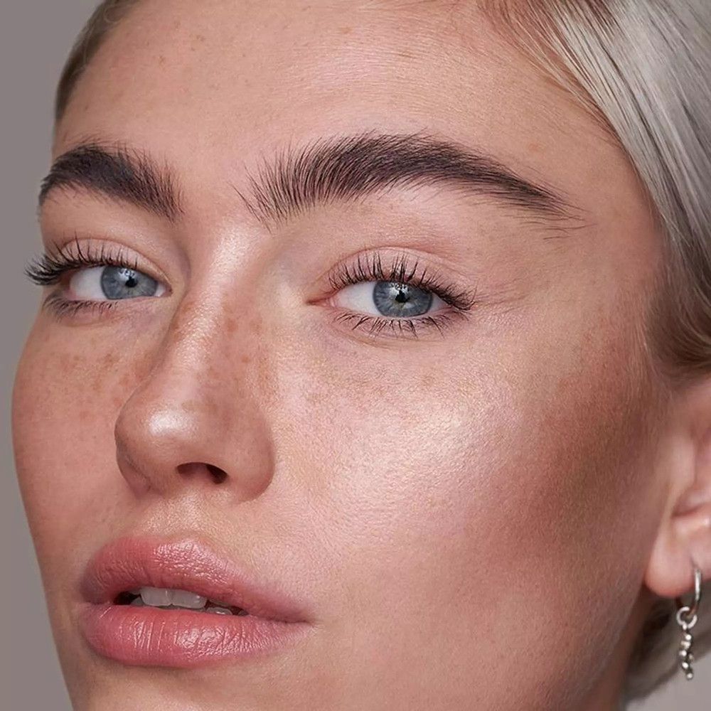 Primo piano di un viso con occhi blu, capelli biondi e lentiggini. La pelle ha una luminosità naturale.