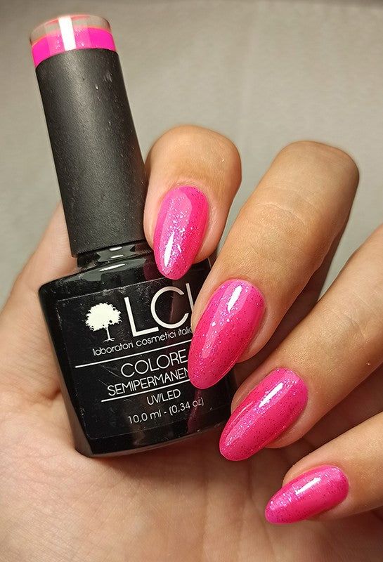 Mano con unghie smaltate e flacone di smalto. Smalto rosa sulle unghie. Flacone nero con etichetta e logo.