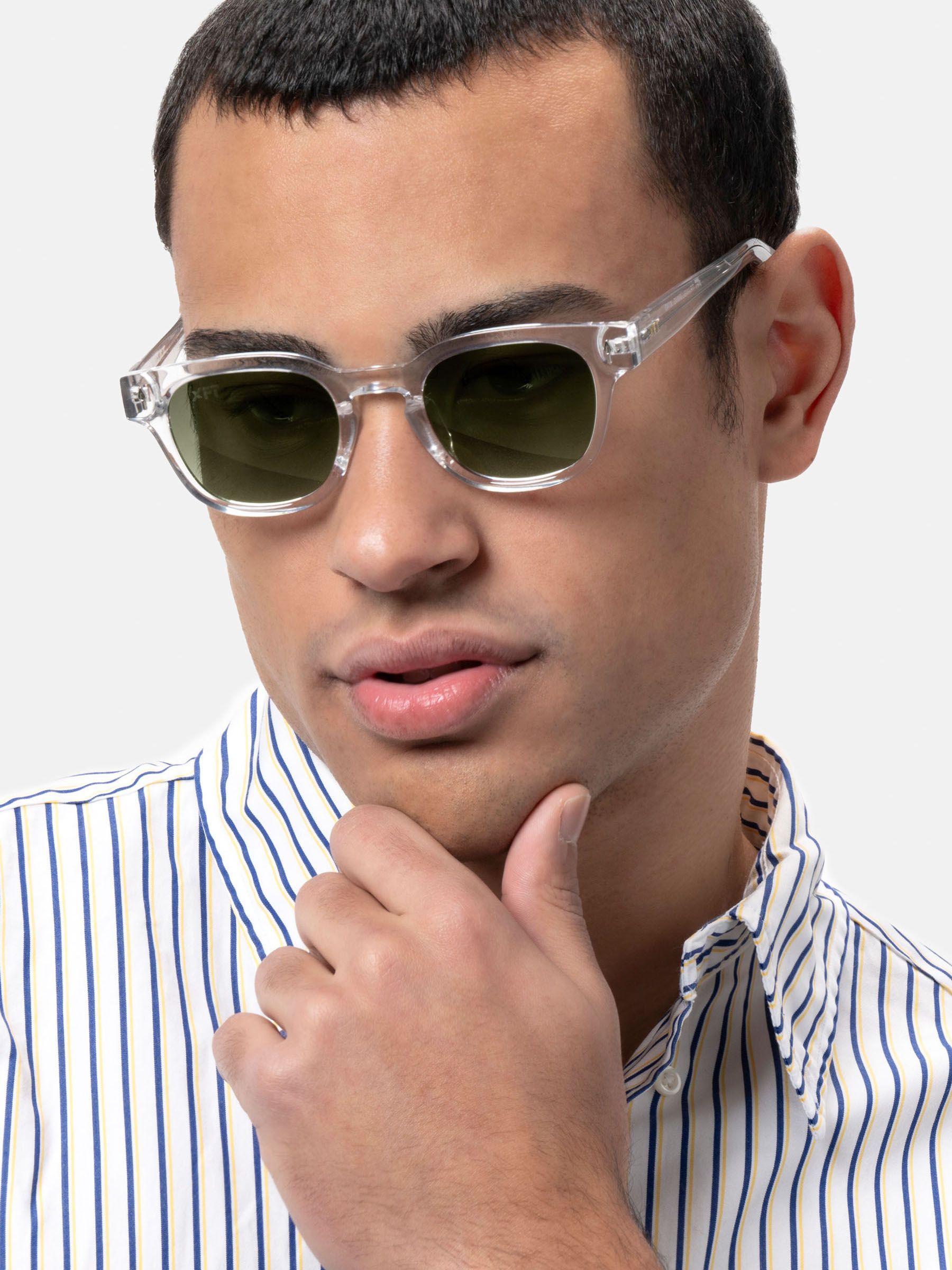 Uomo con occhiali da sole trasparenti e lenti verdi. Primo piano, camicia chiara a righe.