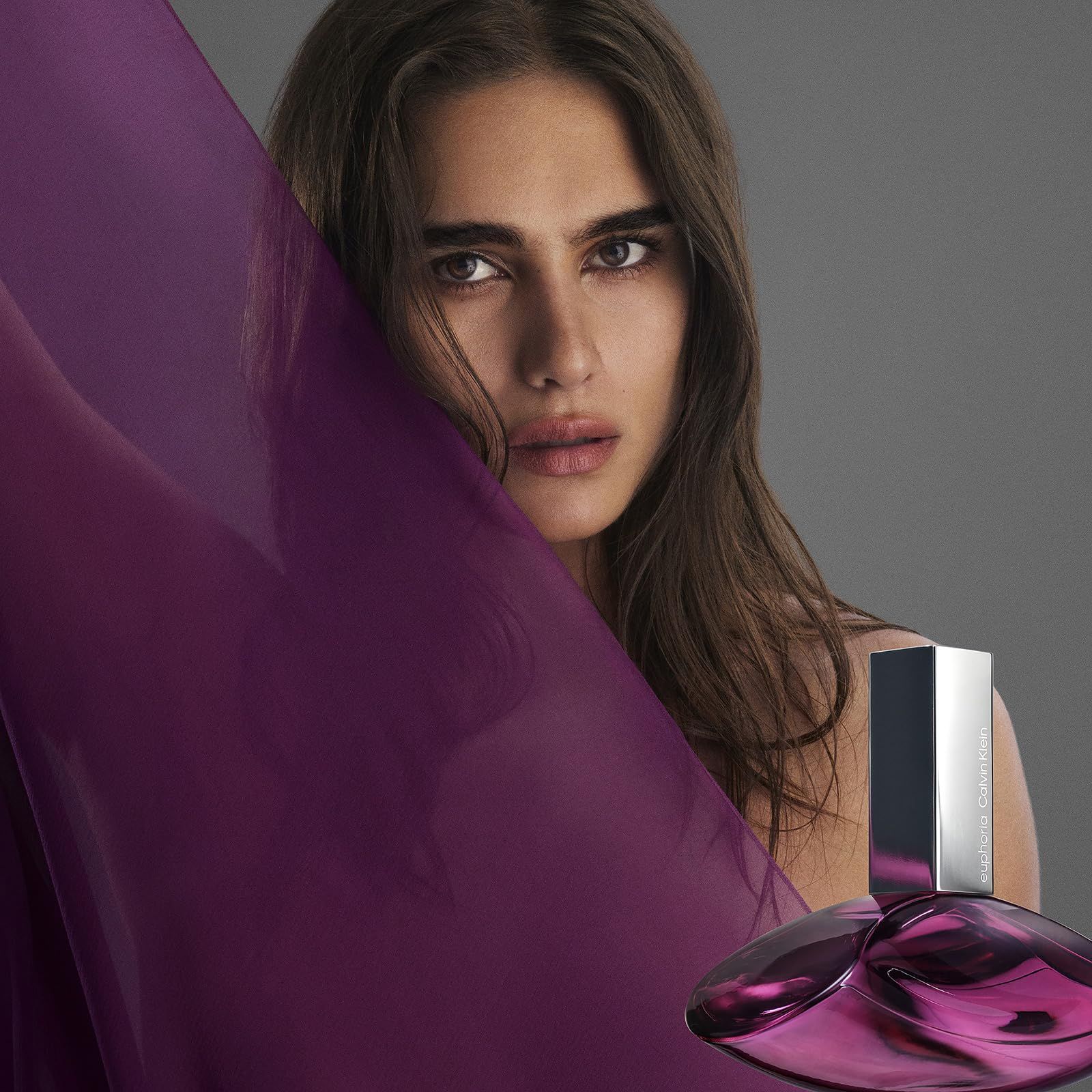Donna con tessuto viola e flacone di profumo. Flacone a goccia, argentato. Donna con tessuto sullo sfondo.