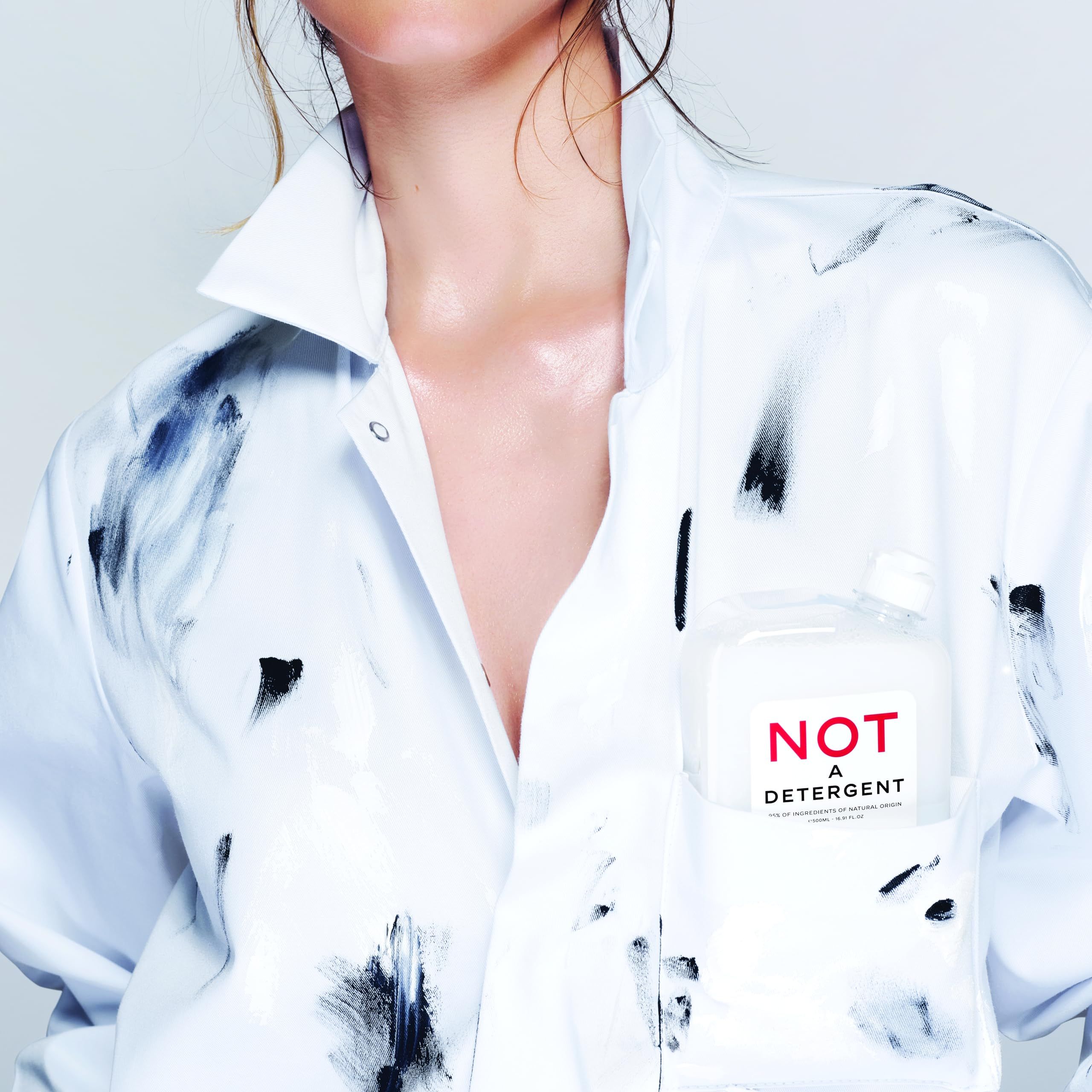 Persona con camicia bianca con schizzi neri. Flacone "NOT A DETERGENT" nella tasca sul petto.