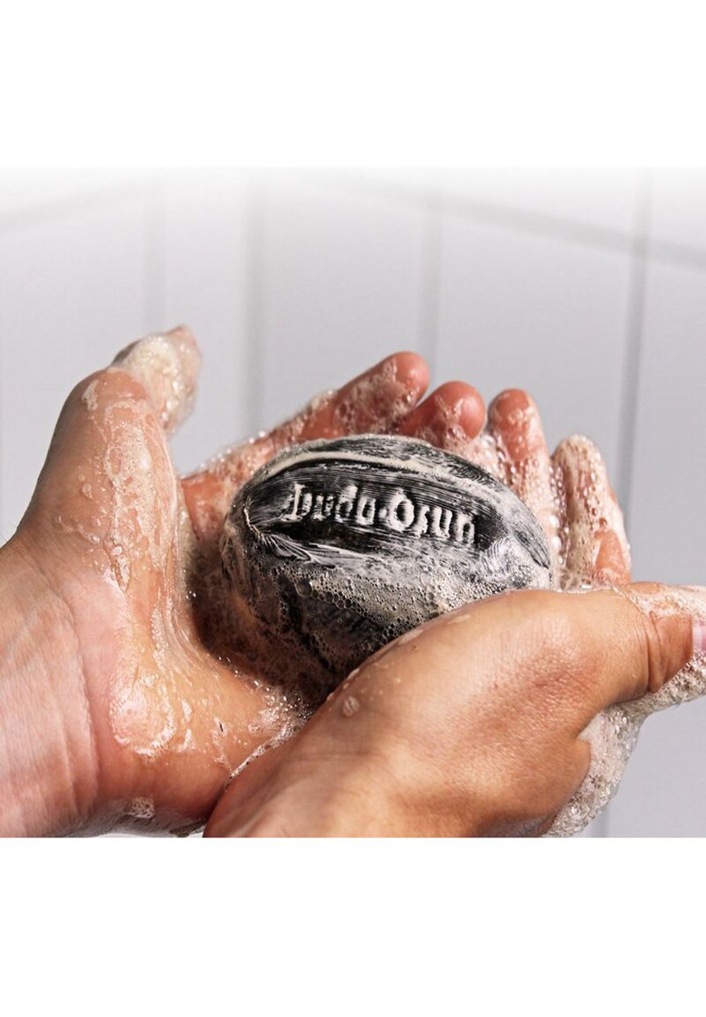 Sapone scuro con scritta in rilievo tra le mani insaponate.