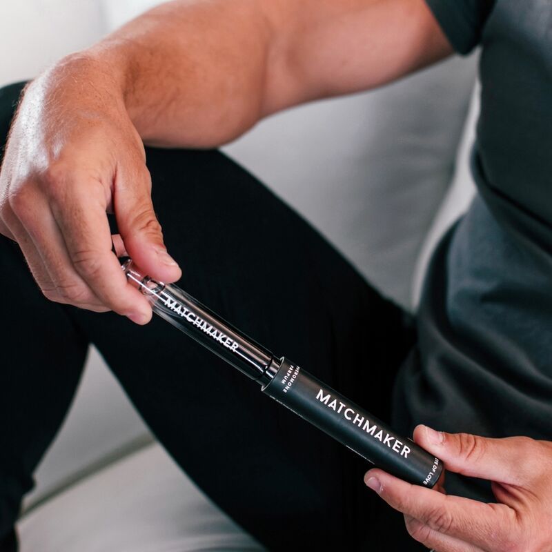 Uomo che tiene la confezione e il flacone. Confezione cilindrica nera e flacone con scritta bianca MATCHMAKER.
