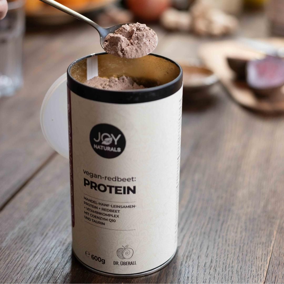 Barattolo beige JOY NATURALS vegan-redbeet:PROTEIN. Cucchiaio con polvere. Scritta: Protein, 600g.