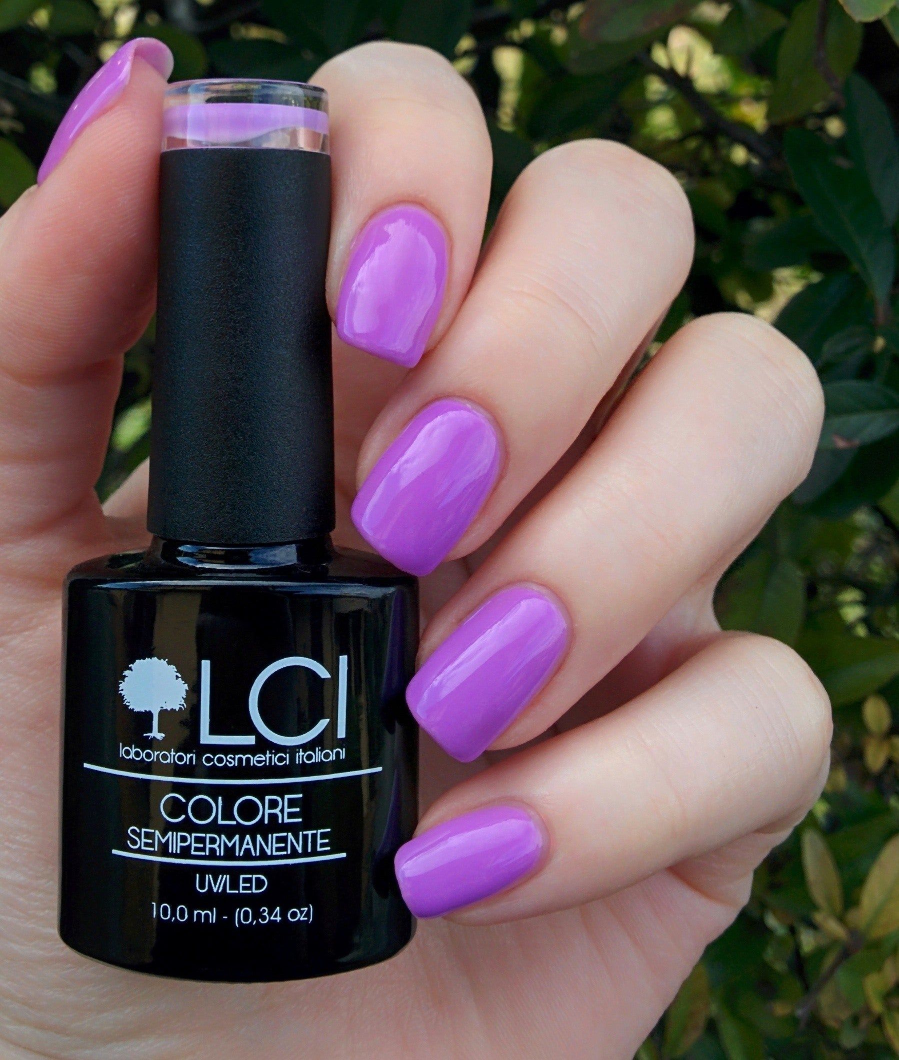 Mano con unghie smaltate e flacone di smalto. Scritta: LCI, Colore Semipermanente, UVLED 10,0 ml. Sfondo: piante.