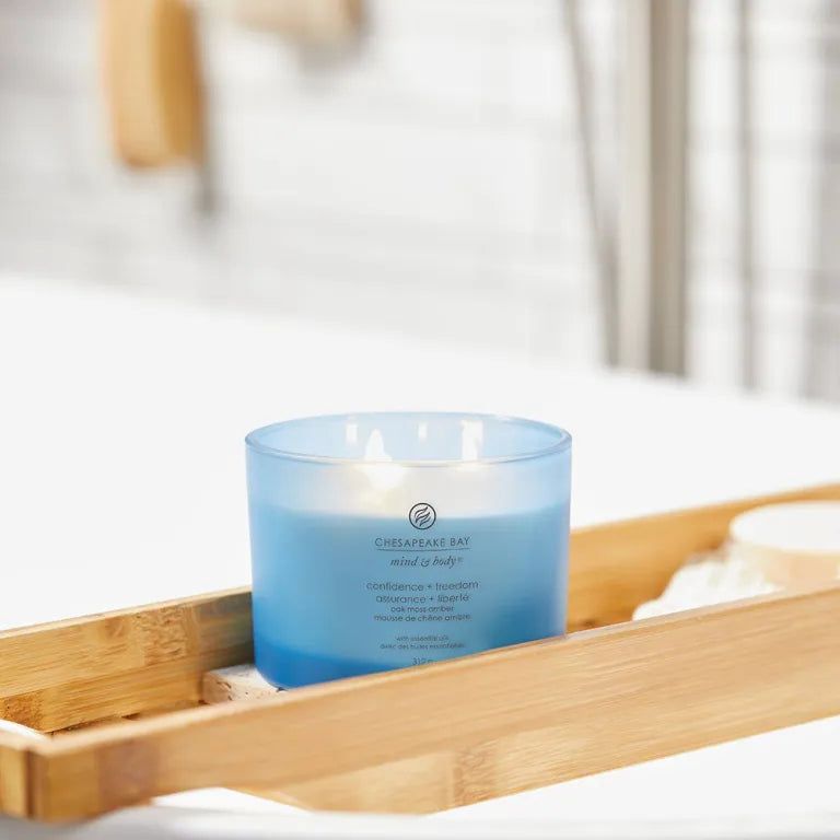 Candela blu Chesapeake Bay, 3 stoppini, su vassoio di legno. Testo: confidence + freedom, assurance + liberté. Contesto bagno.