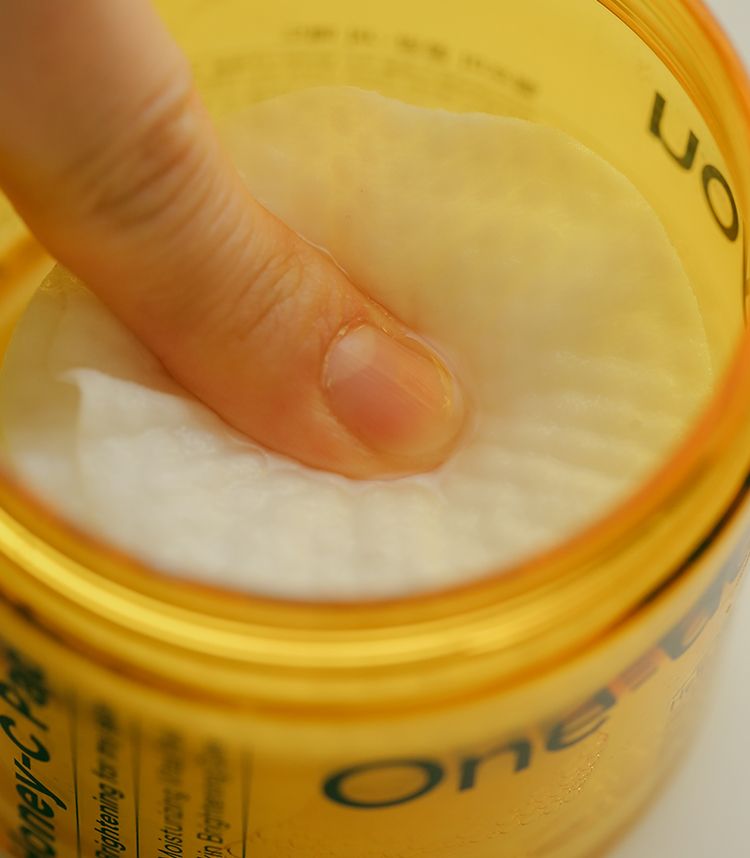 Un dito preme un dischetto di cotone imbevuto in un contenitore giallo.