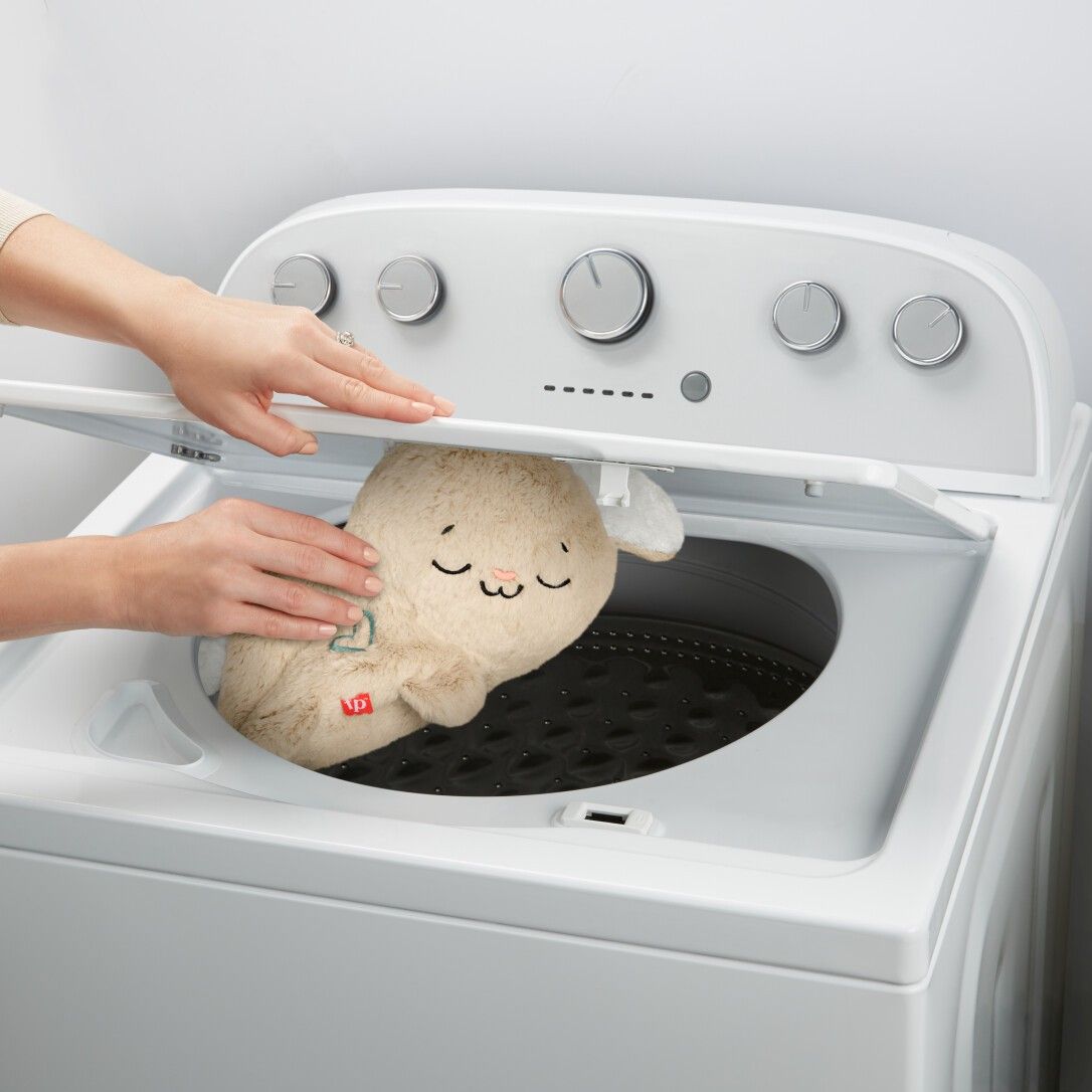 Coniglietto di peluche in lavatrice. Sportello aperto, mani che tengono il giocattolo.