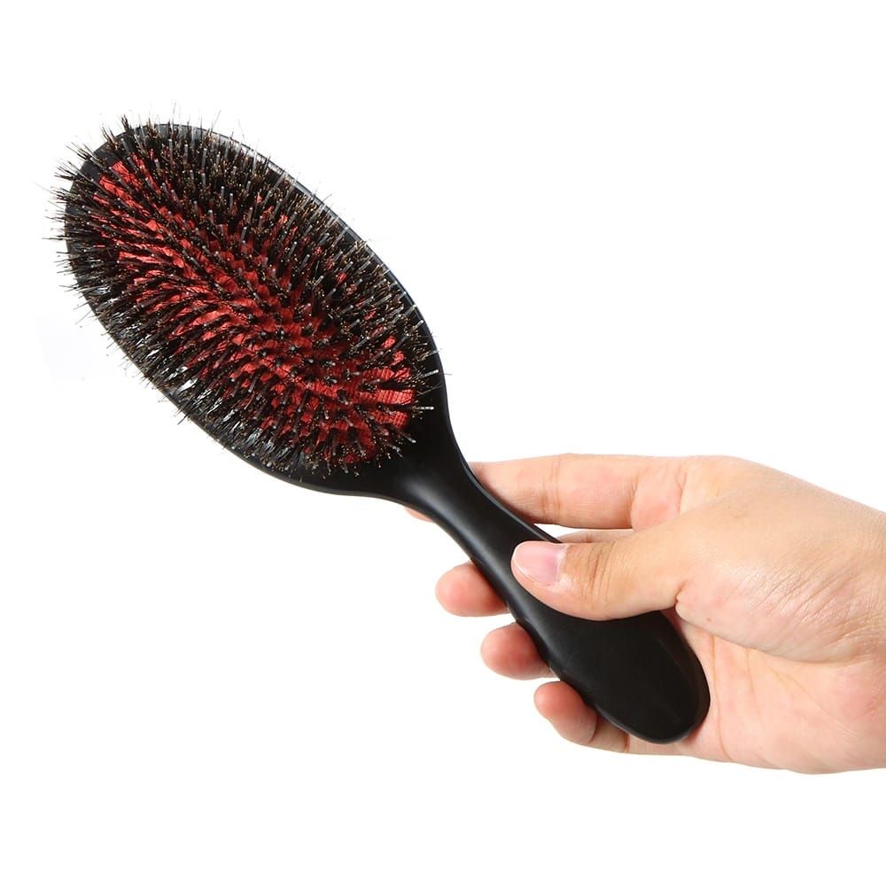 Mano che tiene una spazzola piatta nera con supporto rosso per setole e setole di cinghiale.