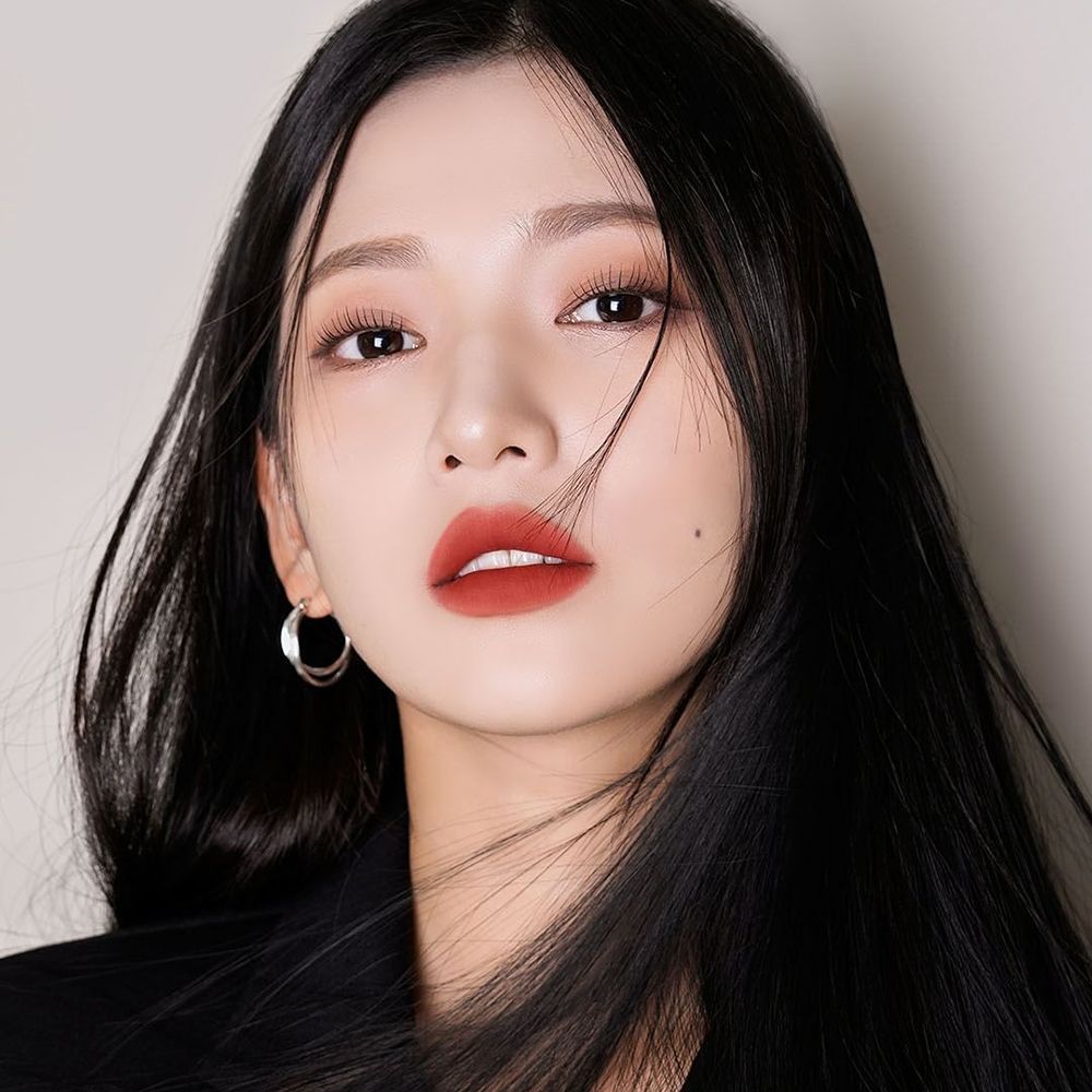 Ritratto di donna con lunghi capelli neri e rossetto rosso. Indossa un blazer nero e orecchini.