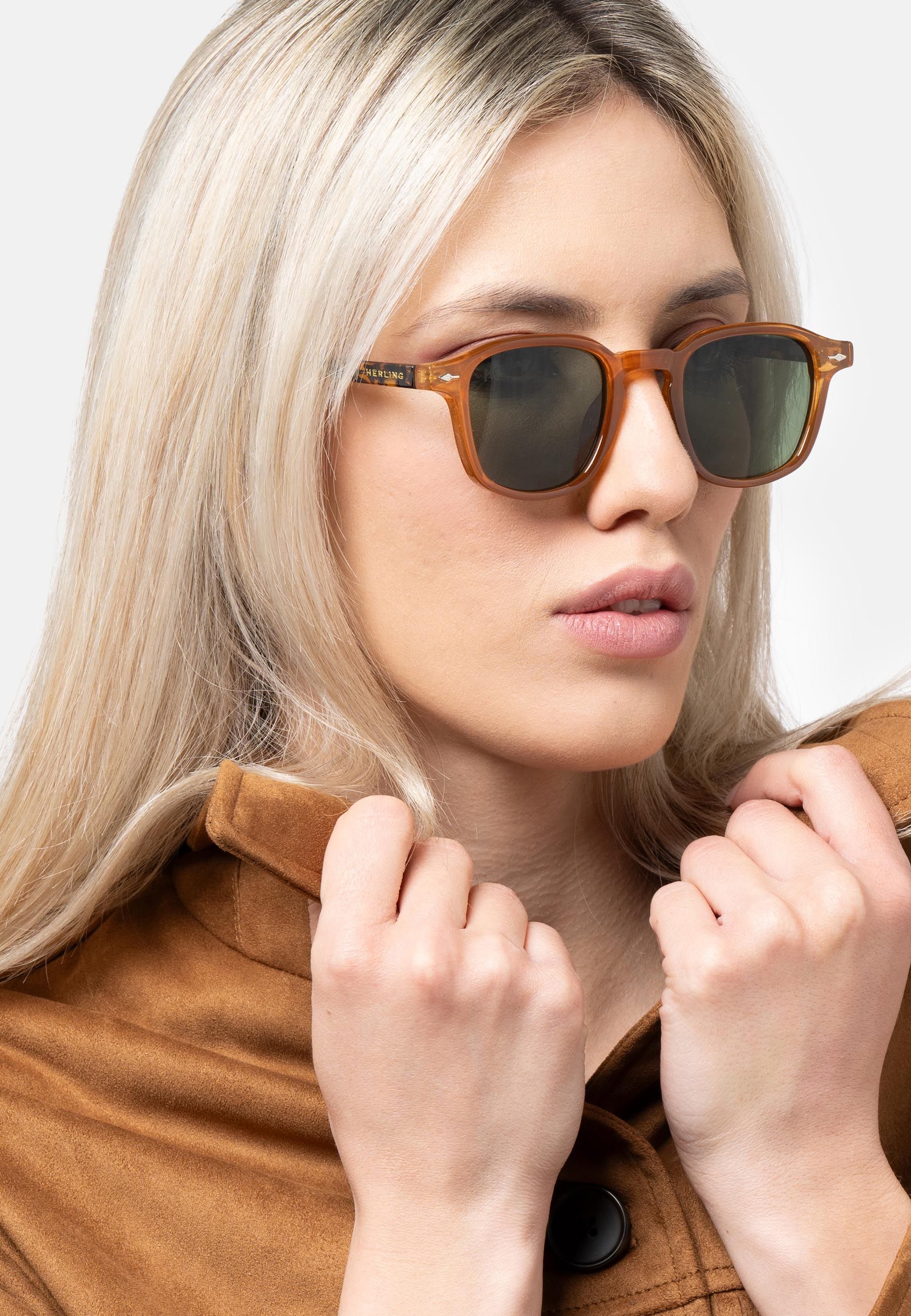Donna con occhiali da sole marroni e lenti verdi. Logo "Herling" sull'asta.