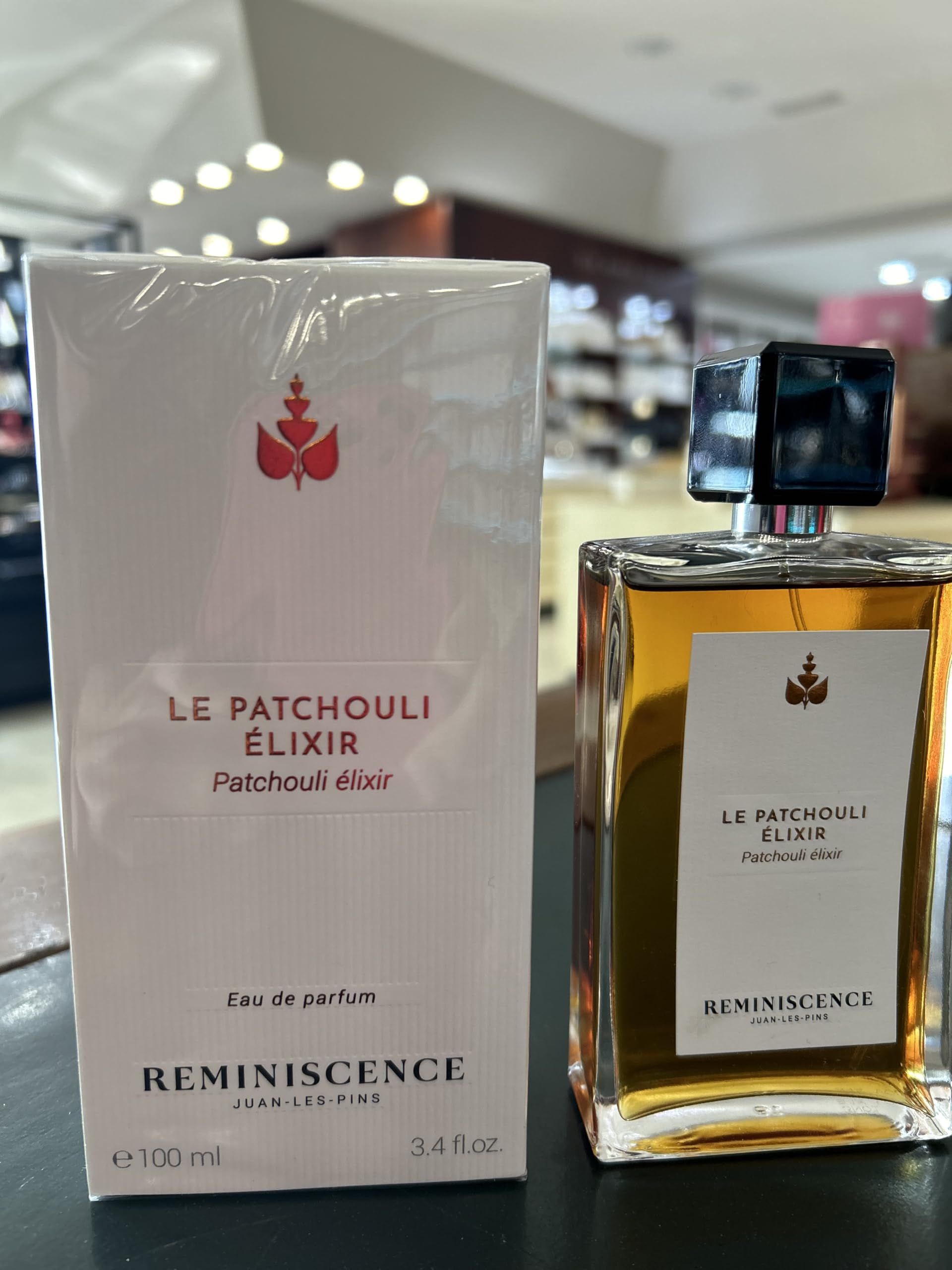 Flacone di profumo e confezione. Flacone con liquido dorato, etichetta bianca. Confezione bianca con logo e testo.