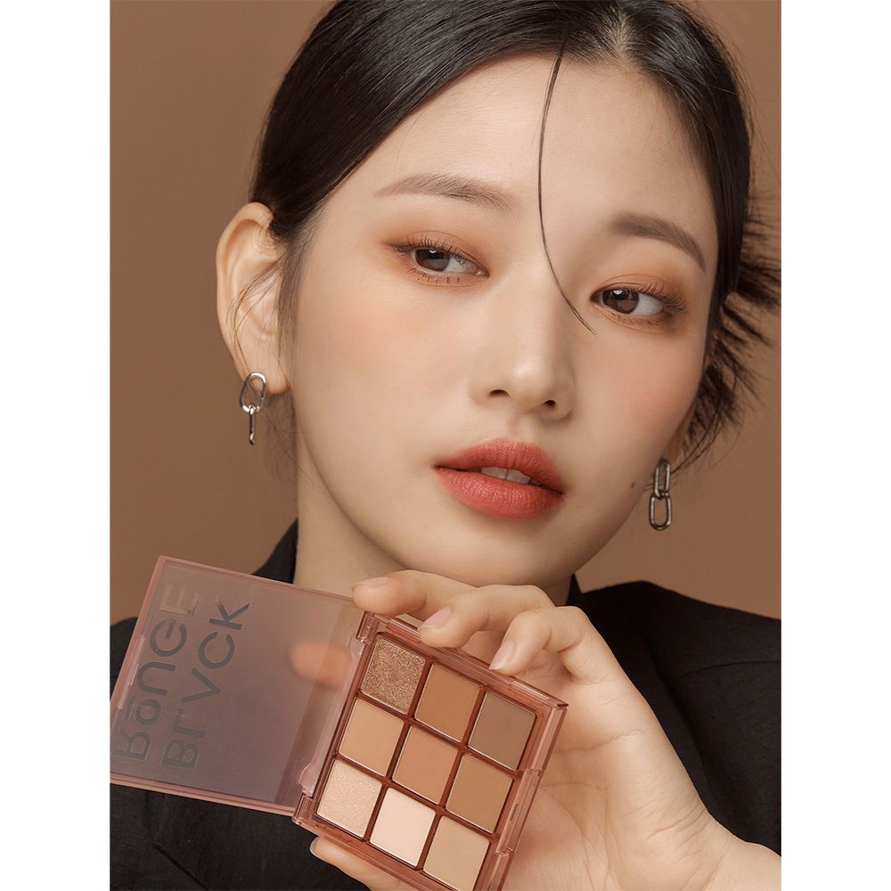 Donna tiene in mano una palette ombretti. Palette con nove tonalità marroni e beige. Confezione trasparente.