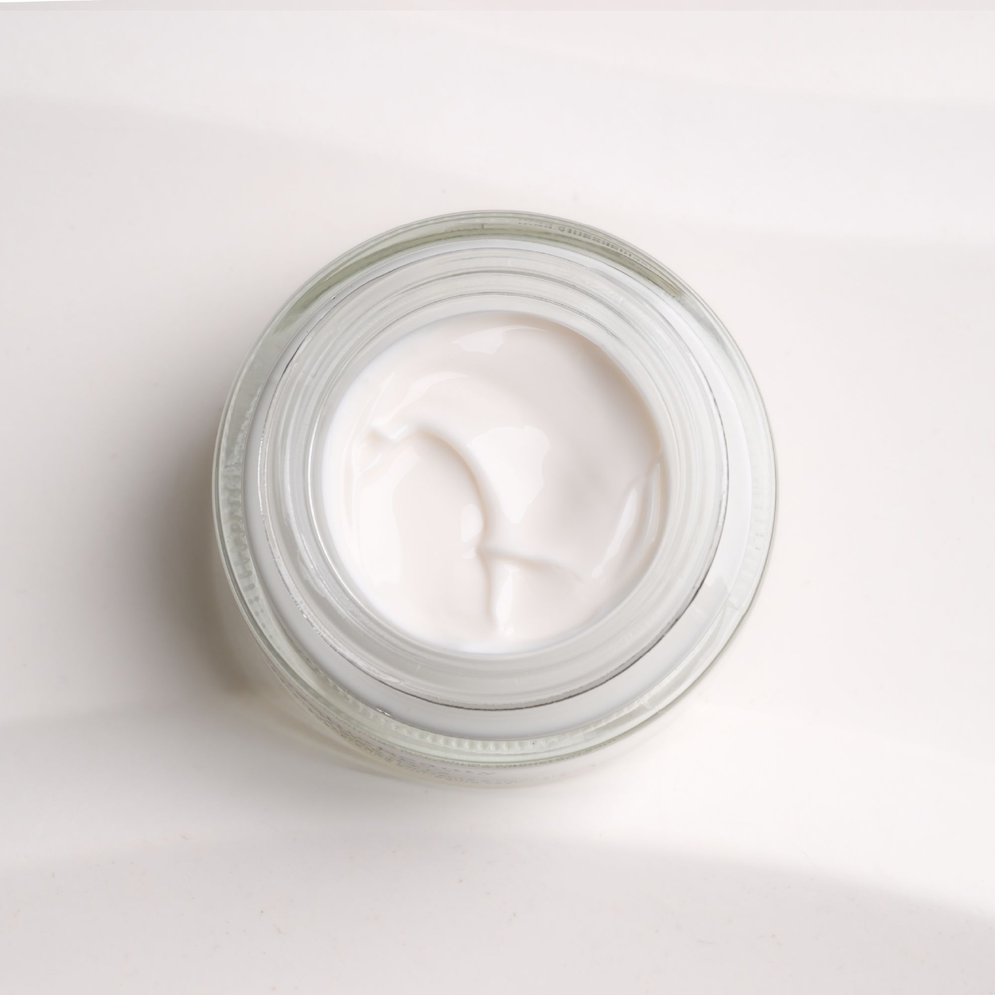 Vaso di crema aperto. Crema color crema in un contenitore di vetro. Vista dall'alto.