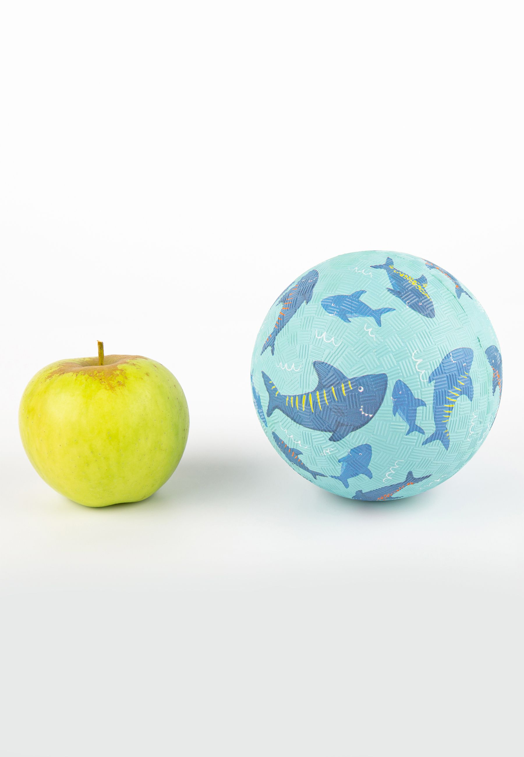 Palla blu con motivo a squalo accanto a una mela. Sfondo azzurro chiaro. Diversi squali di diverse dimensioni e colori.